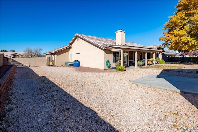 rear view of property featuring a fenced backyard, a tile roof, a chimney, a patio area, and stucco siding