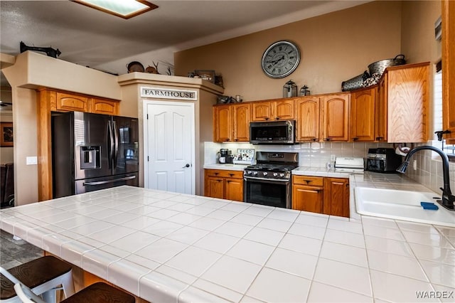 kitchen with tile counters, gas range, vaulted ceiling, refrigerator with ice dispenser, and a sink