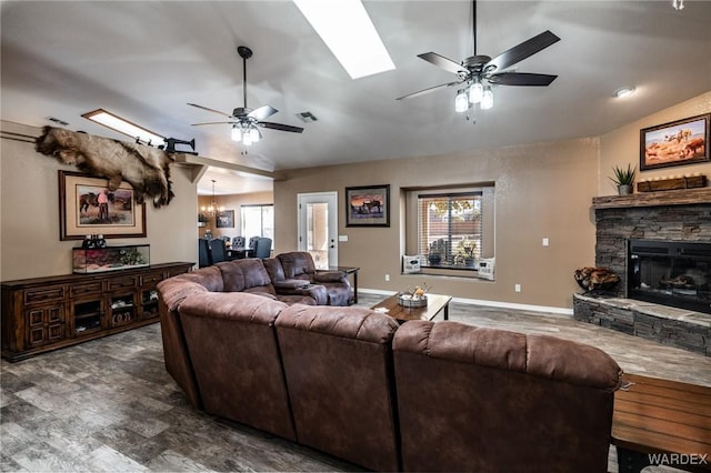 living room with vaulted ceiling with skylight, ceiling fan with notable chandelier, a fireplace, visible vents, and baseboards