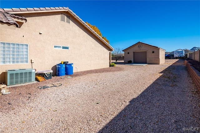 view of property exterior with a detached garage, central air condition unit, stucco siding, fence, and an outdoor structure