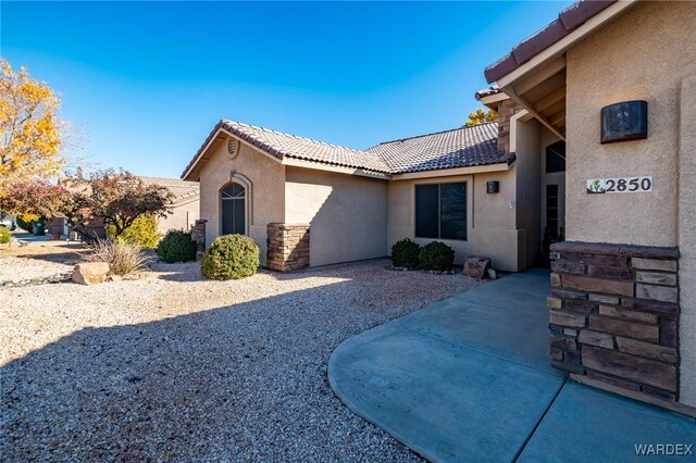 exterior space with stone siding, a tiled roof, a patio area, and stucco siding