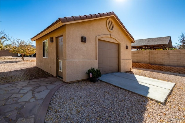 exterior space featuring a garage, an outbuilding, fence, and stucco siding