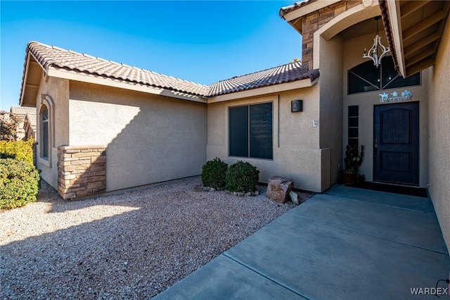 property entrance with stone siding, a tile roof, a patio, and stucco siding