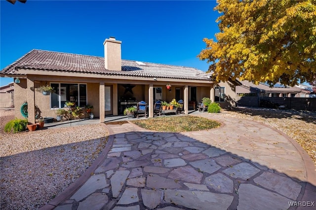 rear view of house with stucco siding, a chimney, fence, and a patio