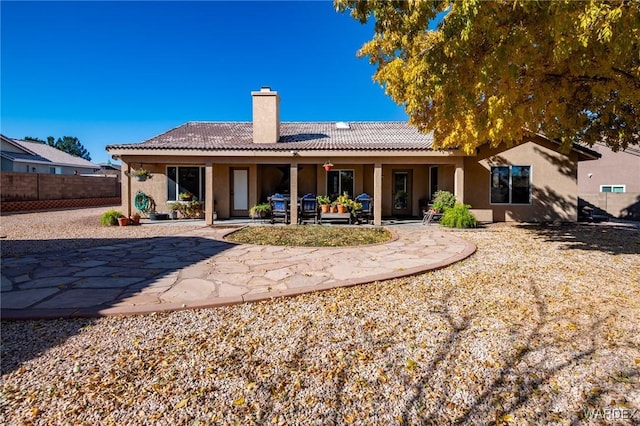 rear view of house with a tiled roof, fence, a chimney, and stucco siding