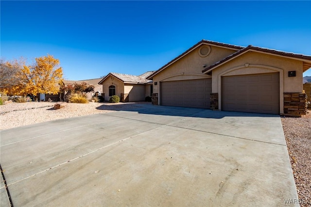 view of front of house featuring a garage, concrete driveway, stone siding, a tile roof, and stucco siding