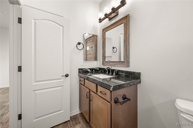 half bathroom with baseboards, vanity, toilet, and wood finished floors