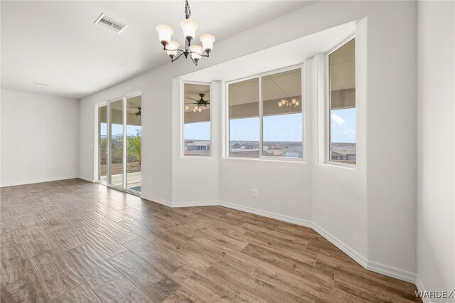 spare room featuring ceiling fan with notable chandelier, visible vents, baseboards, and wood finished floors