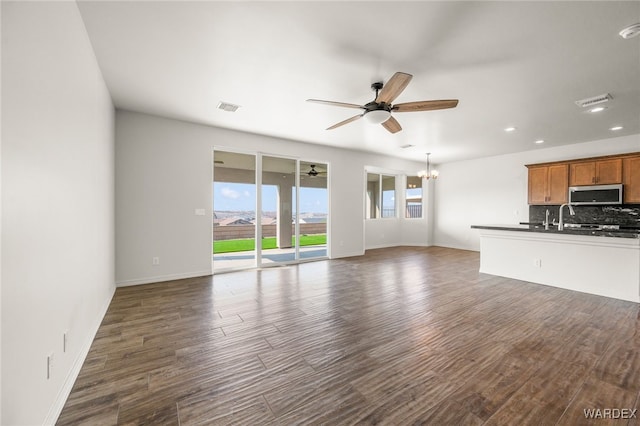 unfurnished living room featuring ceiling fan with notable chandelier, dark wood-style flooring, visible vents, and baseboards