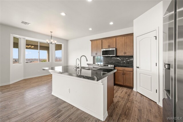 kitchen featuring brown cabinetry, a center island with sink, pendant lighting, and stainless steel appliances