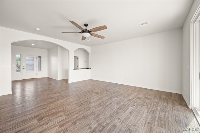 unfurnished living room featuring a ceiling fan, arched walkways, visible vents, and wood finished floors