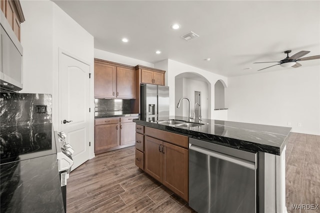 kitchen featuring a sink, visible vents, appliances with stainless steel finishes, brown cabinetry, and an island with sink