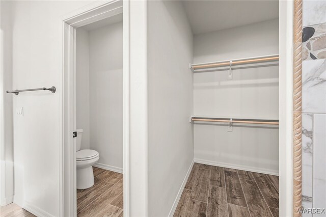 bathroom with a walk in closet, toilet, baseboards, and wood finished floors