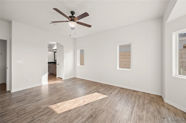 unfurnished bedroom featuring arched walkways, wood finished floors, visible vents, and baseboards