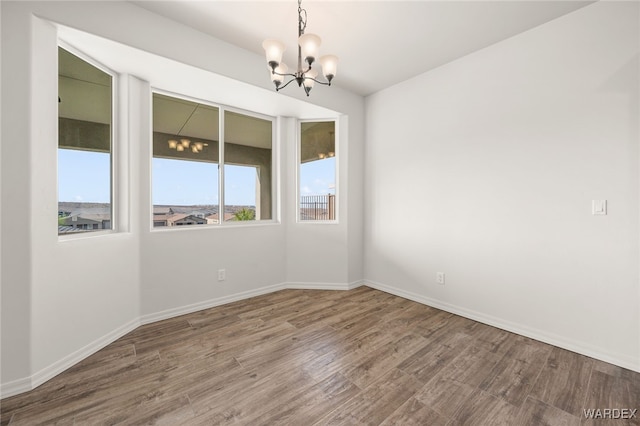 empty room with a notable chandelier, baseboards, and wood finished floors