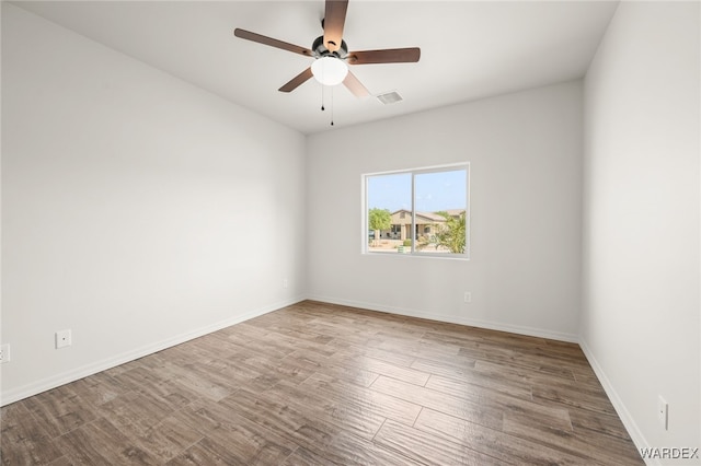 empty room featuring a ceiling fan, visible vents, baseboards, and wood finished floors