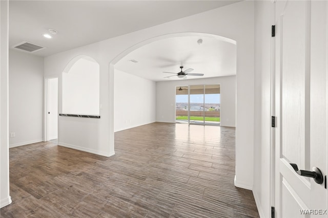 spare room featuring ceiling fan, arched walkways, wood finished floors, visible vents, and baseboards