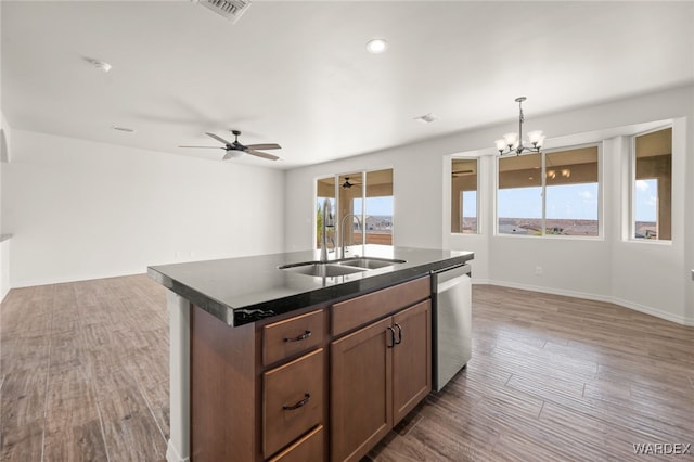 kitchen featuring dark countertops, hanging light fixtures, stainless steel dishwasher, a kitchen island with sink, and a sink