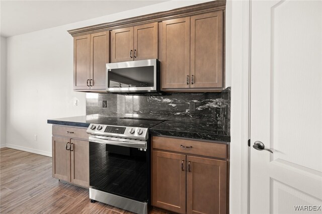 kitchen with tasteful backsplash, baseboards, dark stone counters, appliances with stainless steel finishes, and wood finished floors