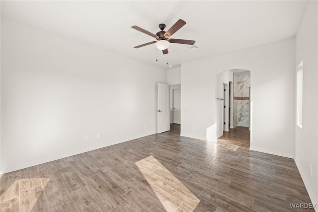 unfurnished bedroom featuring visible vents, arched walkways, baseboards, dark wood-style floors, and ceiling fan