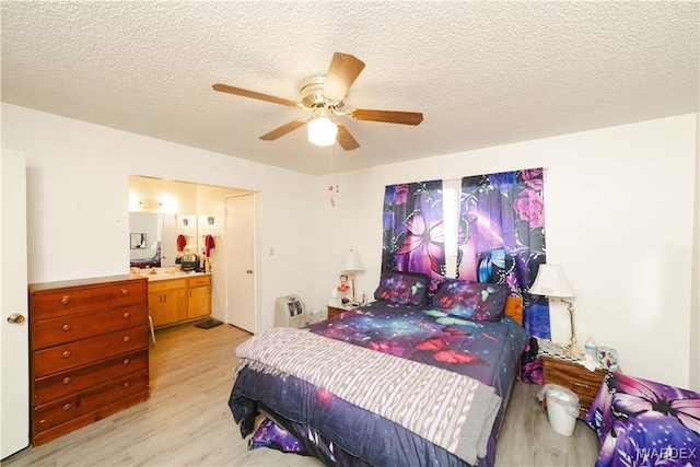 bedroom featuring light wood finished floors, ensuite bath, ceiling fan, and a textured ceiling