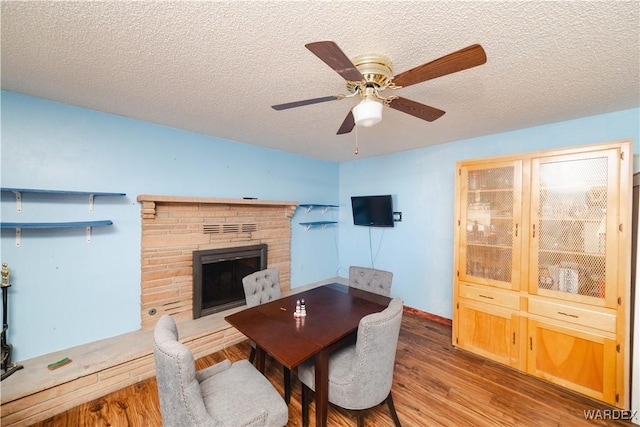 dining area with a fireplace with raised hearth, a textured ceiling, wood finished floors, and a ceiling fan