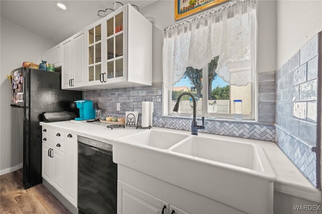 kitchen with a sink, white cabinetry, light countertops, black appliances, and glass insert cabinets