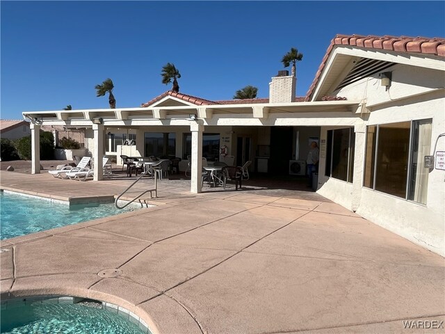 rear view of house with a tile roof, a patio area, a chimney, and a community pool