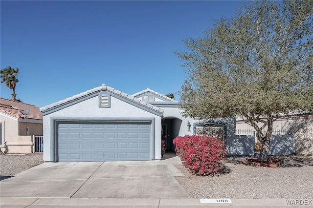 view of front facade with concrete driveway, a tiled roof, an attached garage, fence, and stucco siding