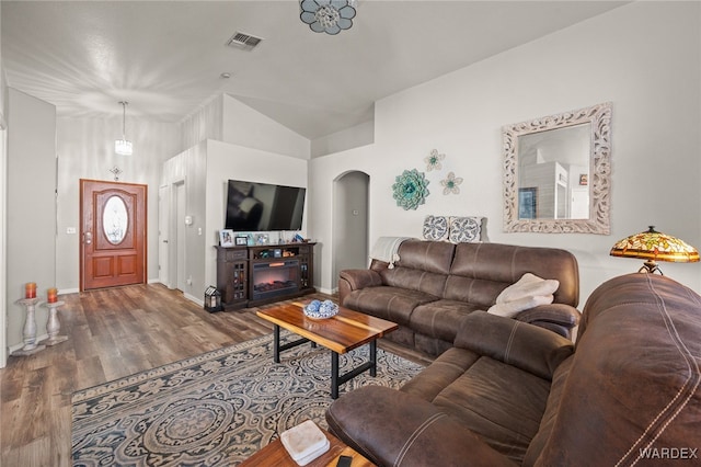 living room featuring arched walkways, visible vents, a glass covered fireplace, wood finished floors, and baseboards