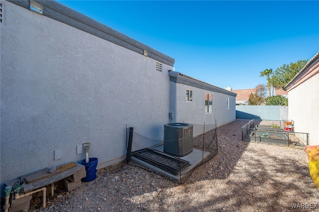 view of home's exterior featuring a garden, fence, central AC unit, and stucco siding