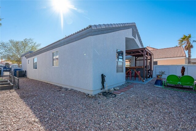 view of side of home featuring central AC unit, fence, a patio, and stucco siding