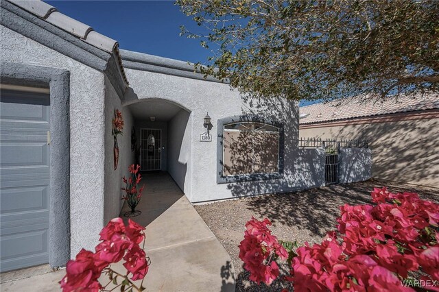 view of exterior entry with a garage, fence, and stucco siding