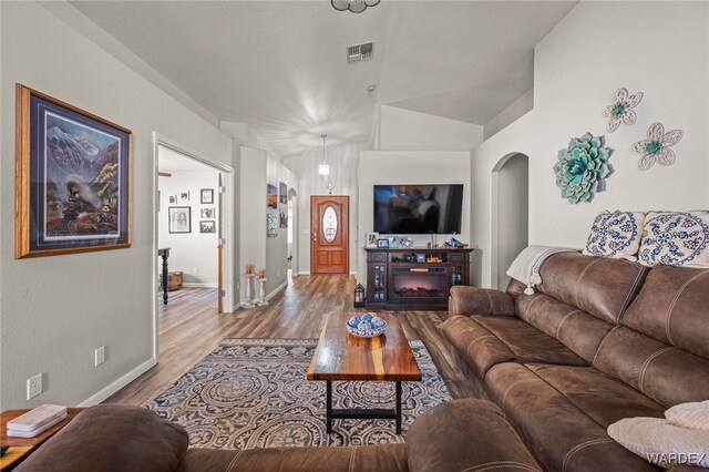 living room with lofted ceiling, arched walkways, wood finished floors, visible vents, and baseboards