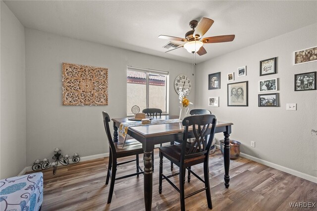 dining space with baseboards, visible vents, ceiling fan, and wood finished floors