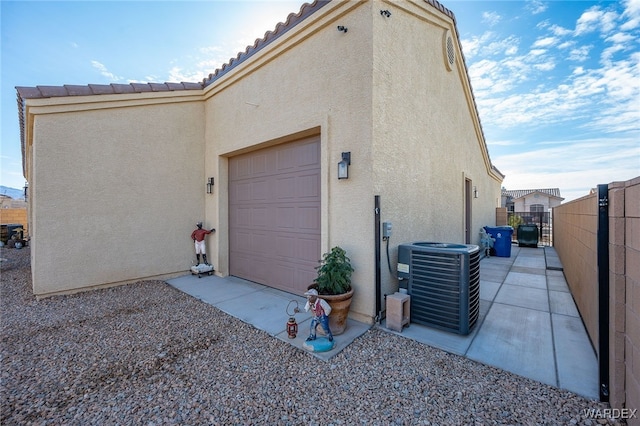 exterior space featuring cooling unit, fence, an attached garage, and stucco siding