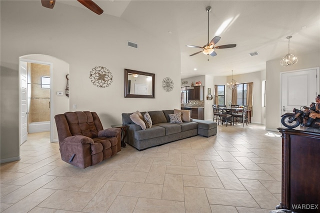 living area featuring high vaulted ceiling, visible vents, arched walkways, and ceiling fan with notable chandelier