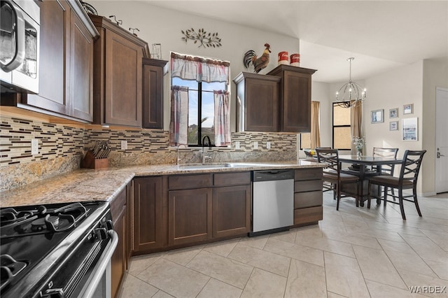 kitchen featuring dark brown cabinetry, appliances with stainless steel finishes, light stone counters, hanging light fixtures, and a sink