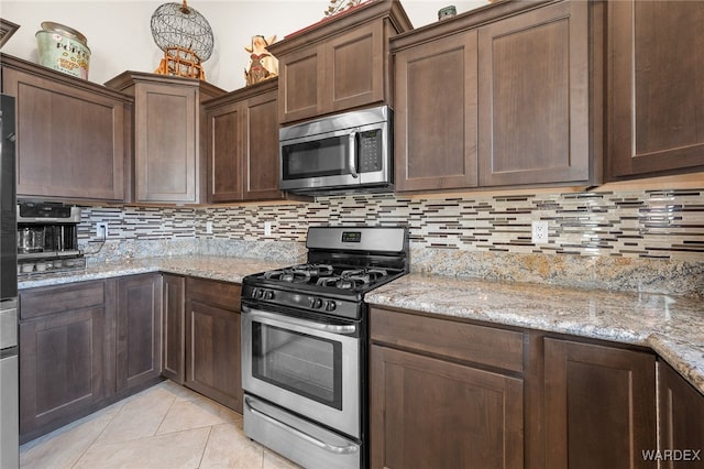 kitchen featuring stainless steel appliances, tasteful backsplash, light tile patterned flooring, dark brown cabinetry, and light stone countertops