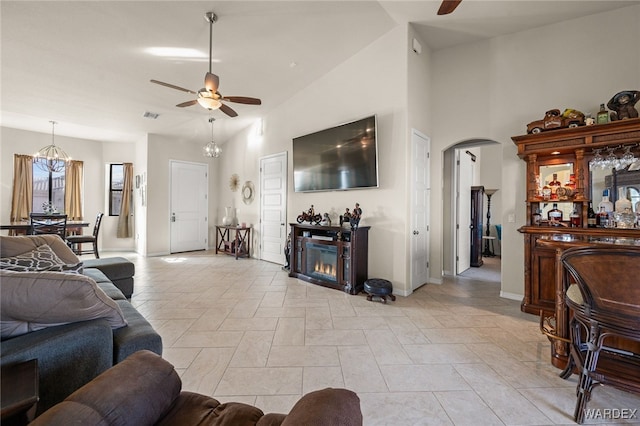 living room featuring arched walkways, high vaulted ceiling, ceiling fan with notable chandelier, baseboards, and a glass covered fireplace