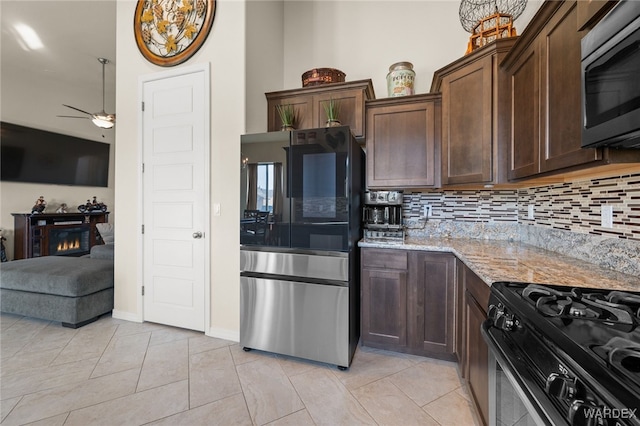 kitchen with tasteful backsplash, light stone countertops, a lit fireplace, stainless steel appliances, and dark brown cabinets