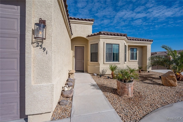 property entrance featuring a garage, a tiled roof, and stucco siding