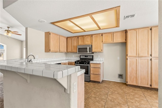 1951 E Oatman Pl, Mohave Valley, AZ 86440 - kitchen featuring appliances with stainless steel finishes, tile counters, a peninsula, and light brown cabinetry
