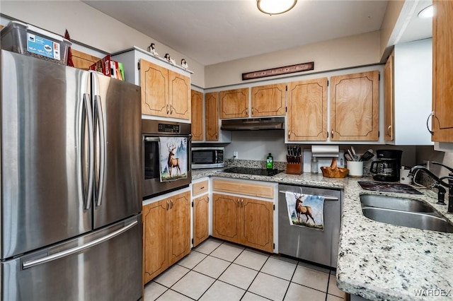 kitchen with light stone countertops, under cabinet range hood, light tile patterned flooring, stainless steel appliances, and a sink