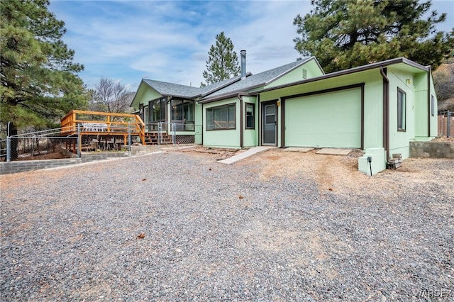 view of front facade featuring fence, a wooden deck, a garage, a sunroom, and driveway