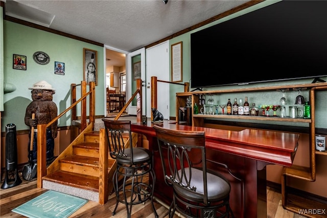 bar with crown molding, stairway, wood finished floors, a textured ceiling, and a bar