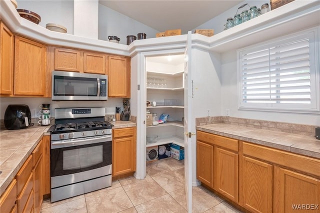 kitchen with tile countertops, appliances with stainless steel finishes, and light tile patterned floors
