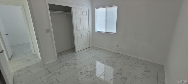 unfurnished bedroom featuring marble finish floor, baseboards, and a closet