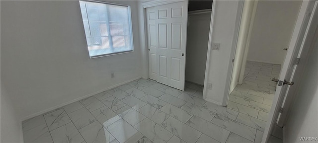 unfurnished bedroom with marble finish floor, baseboards, and a closet