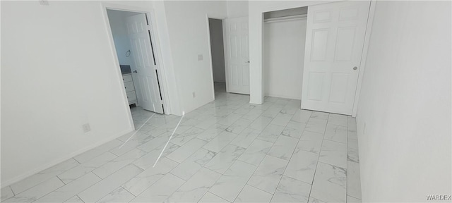 unfurnished bedroom featuring marble finish floor, a closet, connected bathroom, and baseboards